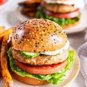 Greek turkey burger on a sesame bun with lettuce, tomato, cucumber, and tzatziki, with another burger in the background.