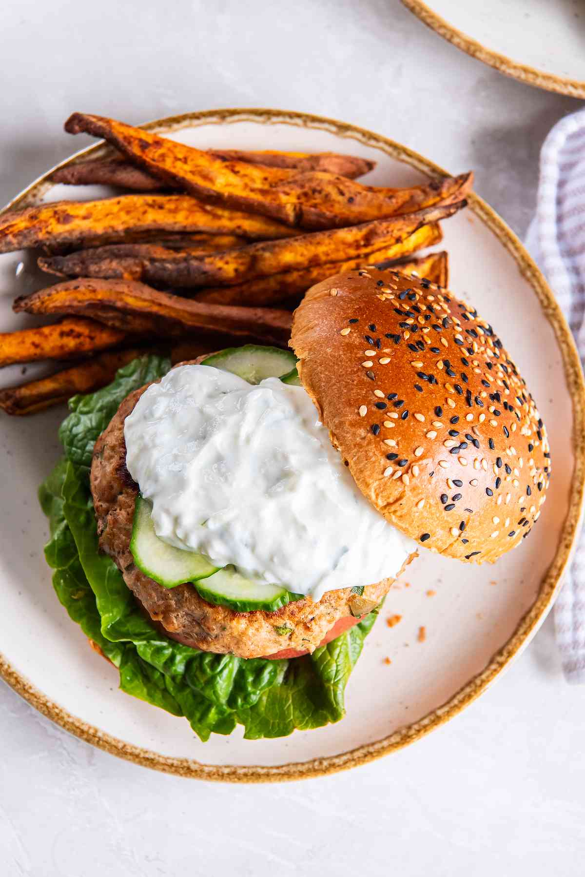 Greek turkey burger topped with cucumber and tzatziki on a sesame bun, served with sweet potato fries.