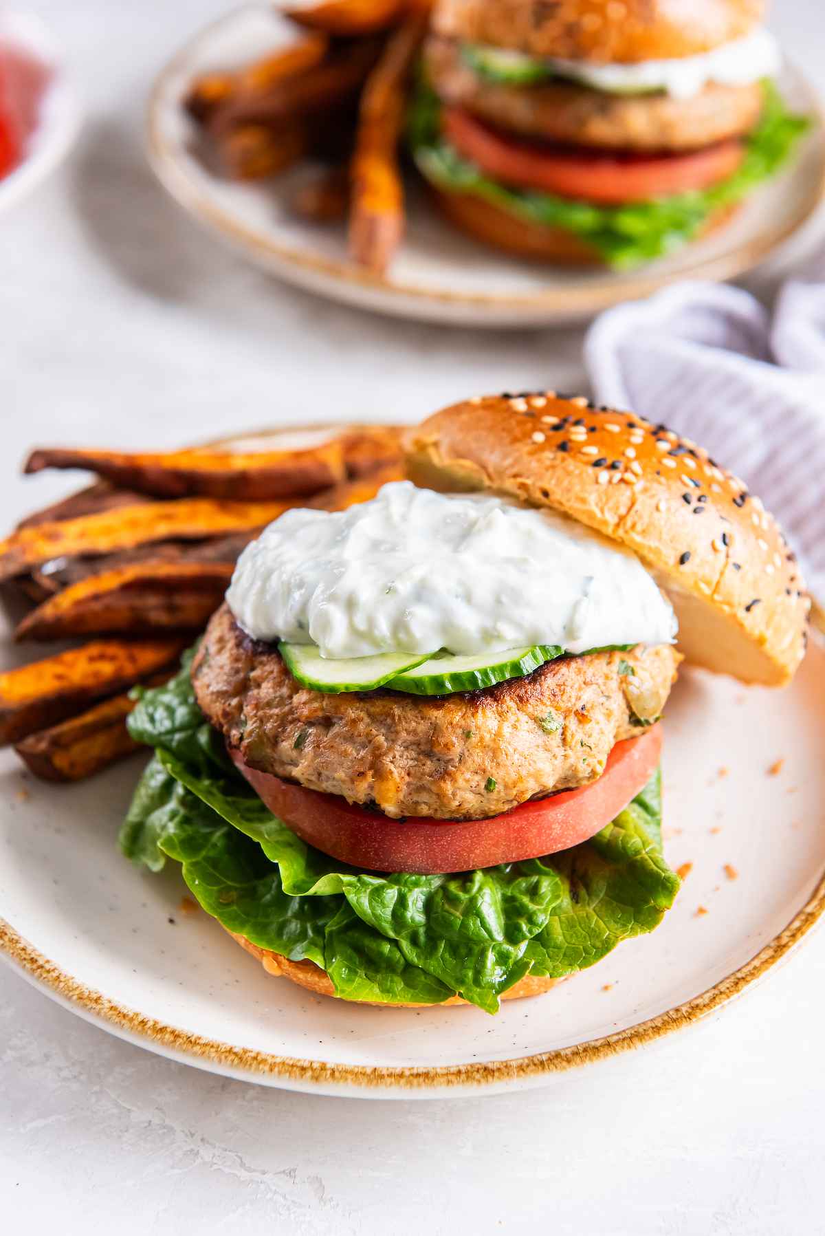 Greek turkey burger on a bun with lettuce, tomato, cucumber, and tzatziki, served with sweet potato fries.