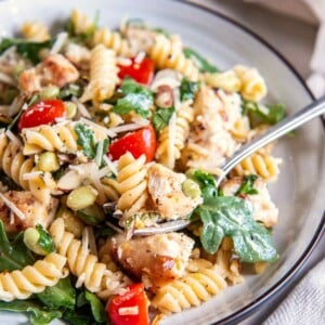 Close-up of lemon basil chicken pasta salad with golden chicken, rotini, arugula, tomatoes, edamame, almonds, and Parmesan.