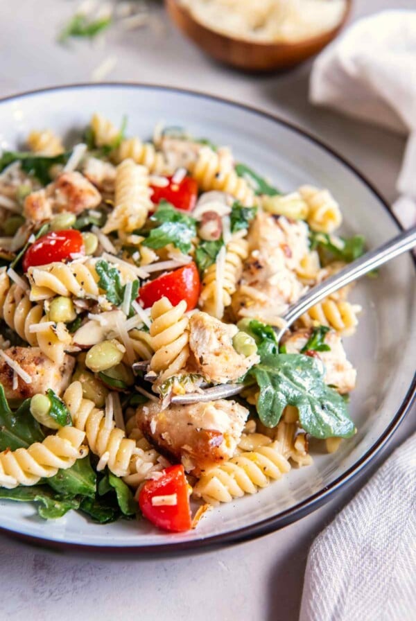 Close-up of lemon basil chicken pasta salad with golden chicken, rotini, arugula, tomatoes, edamame, almonds, and Parmesan.