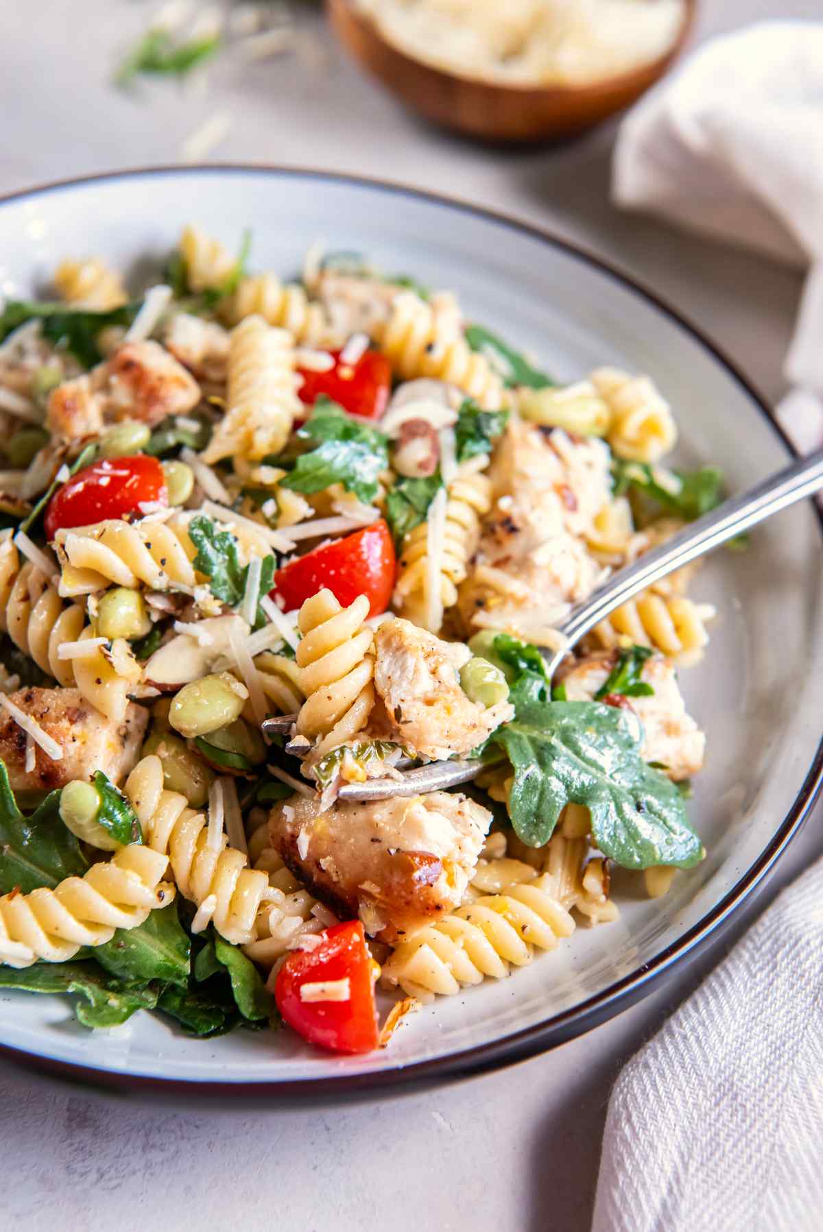 Close-up of lemon basil chicken pasta salad with golden chicken, rotini, arugula, tomatoes, edamame, almonds, and Parmesan.