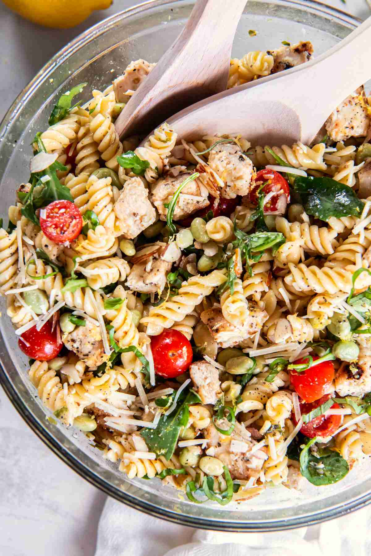 Lemon basil chicken pasta salad tossed in a large bowl with chicken, rotini, arugula, tomatoes, edamame, almonds, and Parmesan.