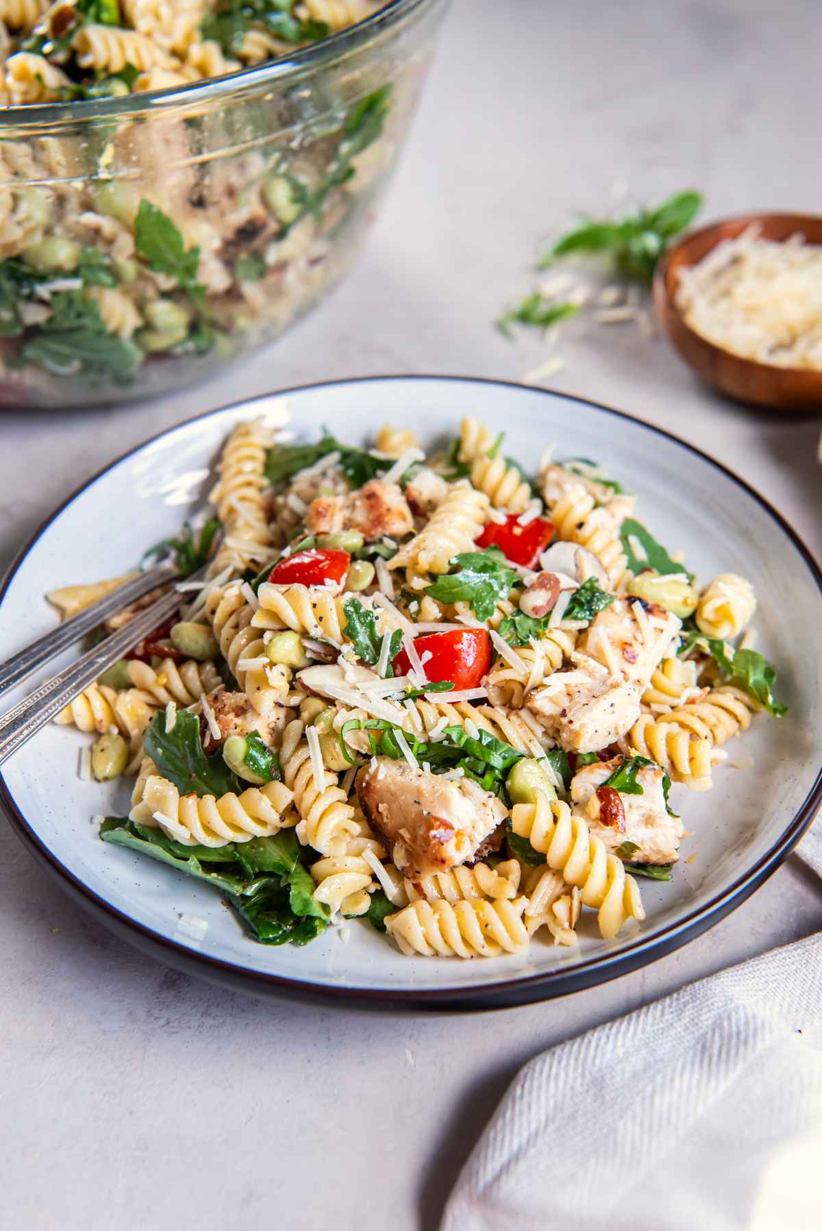 Lemon basil chicken pasta salad served on a plate with rotini, chicken, arugula, edamame, tomatoes, almonds, and Parmesan.