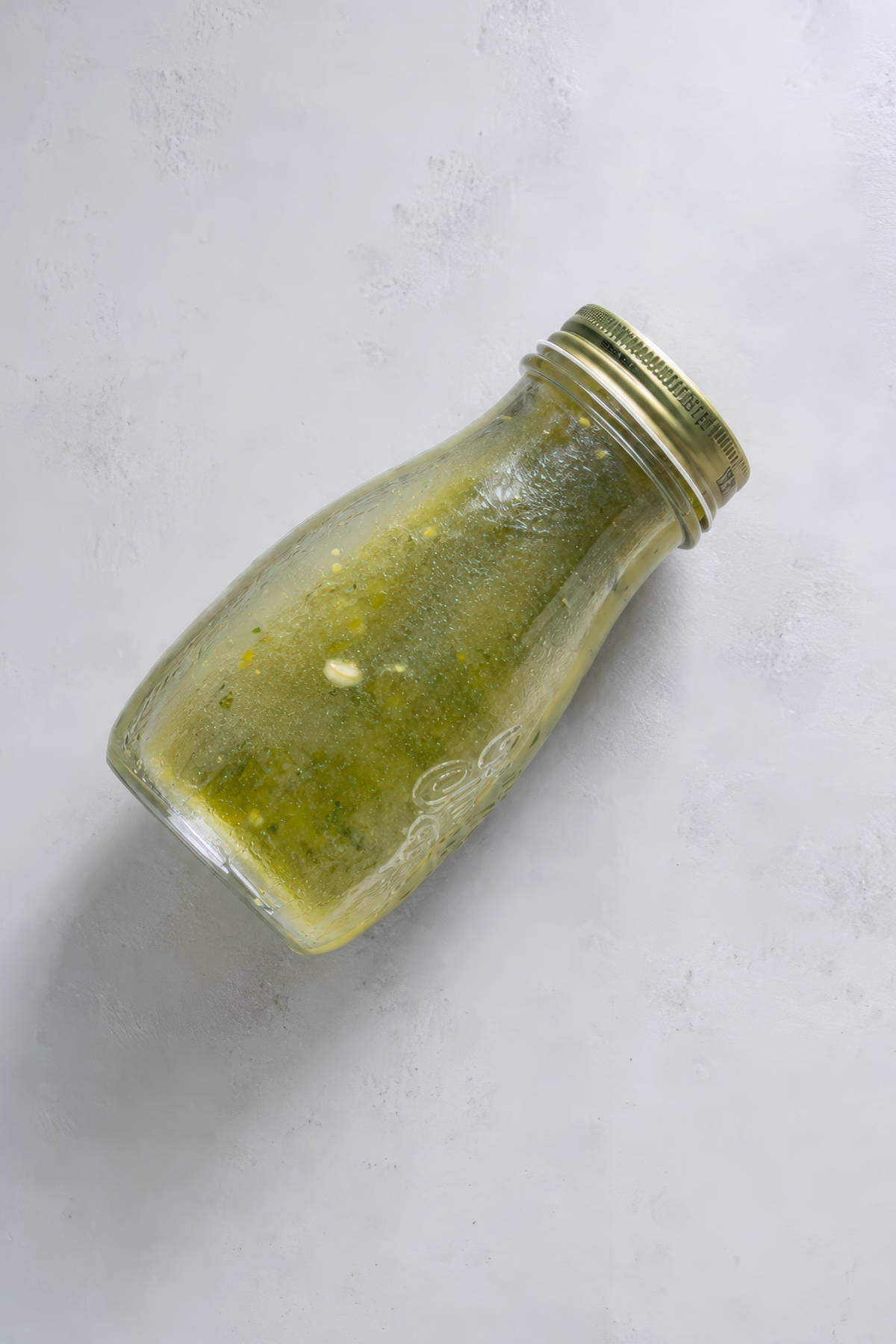 Homemade lemon basil vinaigrette in a glass jar on a light gray surface.