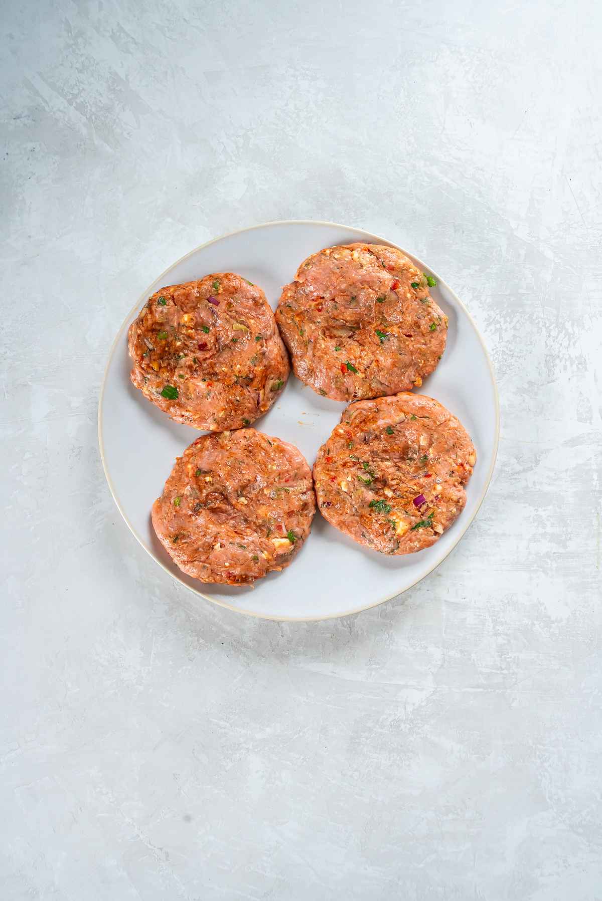 Four shaped Greek turkey burger patties on a plate before chilling.