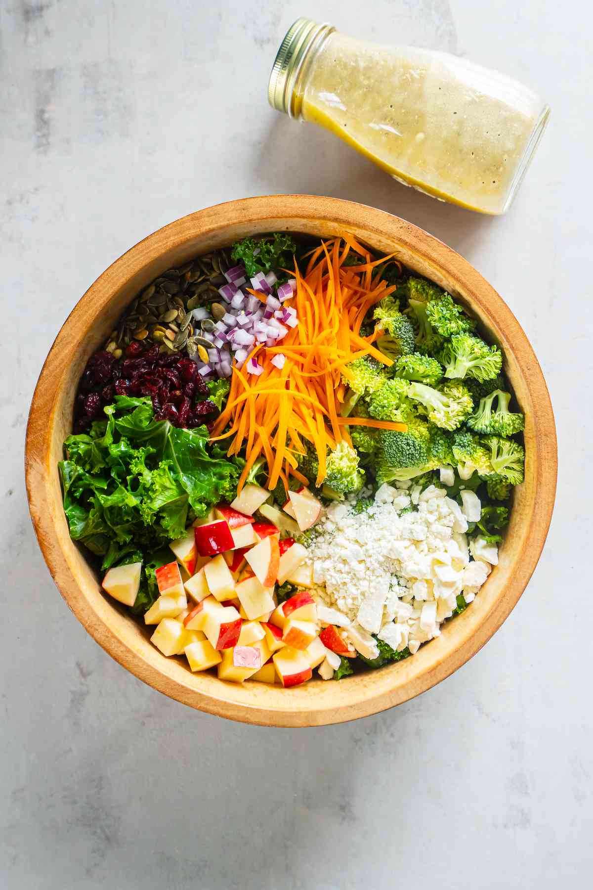 Massaged kale topped with apples, broccoli, carrots, feta, cranberries, pepitas, and red onion before tossing.