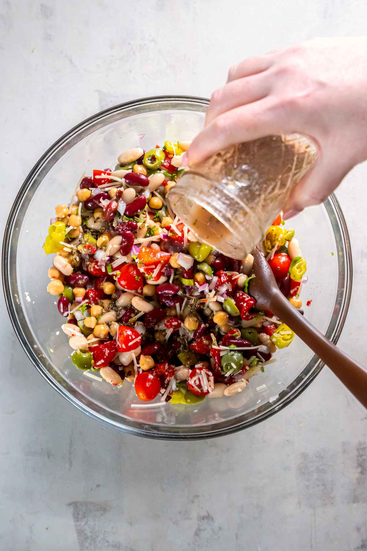 Red wine vinaigrette being poured over Italian three bean salad in a glass mixing bowl.