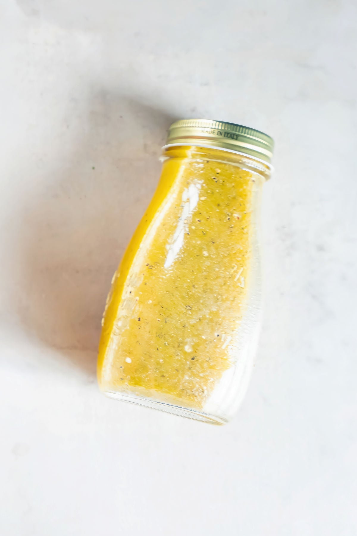 Jar of homemade apple cider vinaigrette with visible Dijon mustard, garlic, and black pepper.