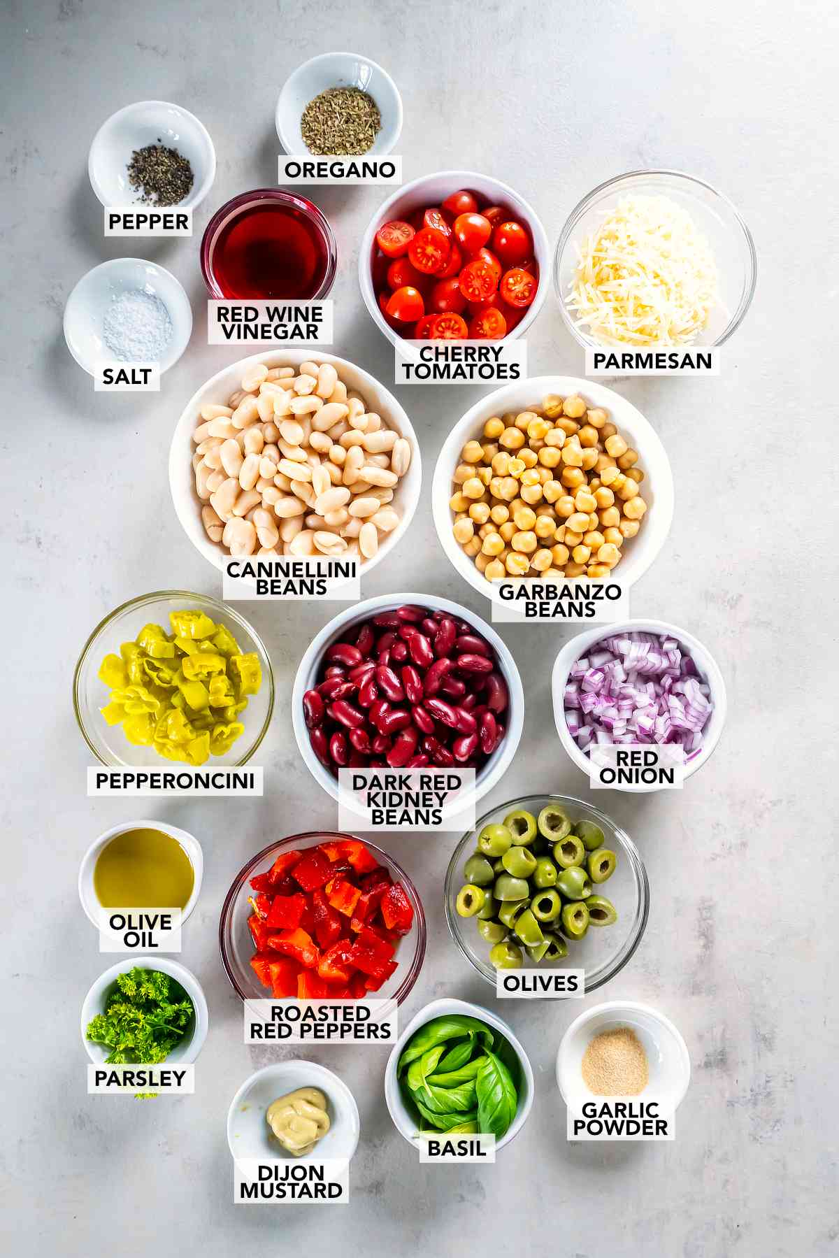 Labeled Italian three bean salad ingredients, including chickpeas, cannellini beans, kidney beans, tomatoes, peppers, olives, Parmesan, herbs, and vinaigrette ingredients.