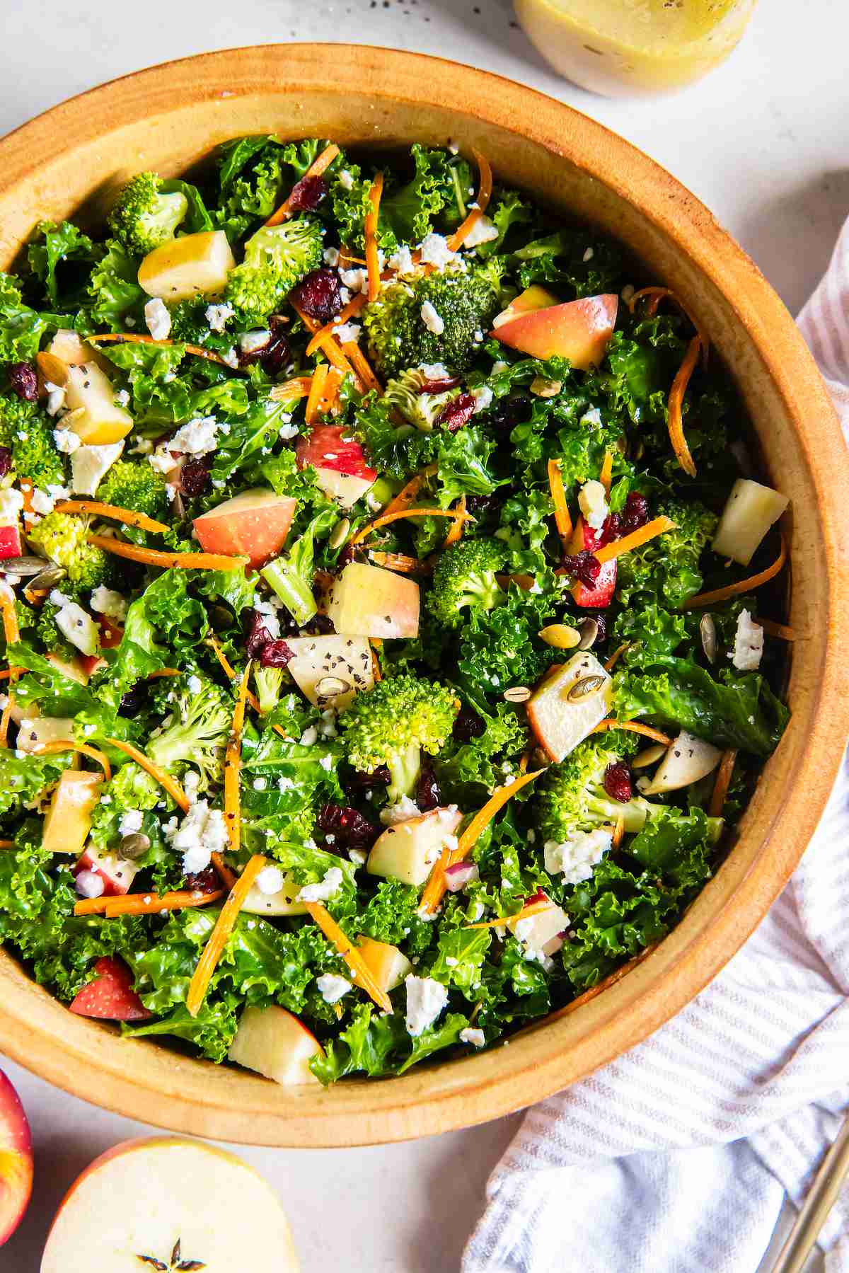 Overhead view of kale apple salad with crisp apples, broccoli, feta, carrots, cranberries, and pumpkin seeds.