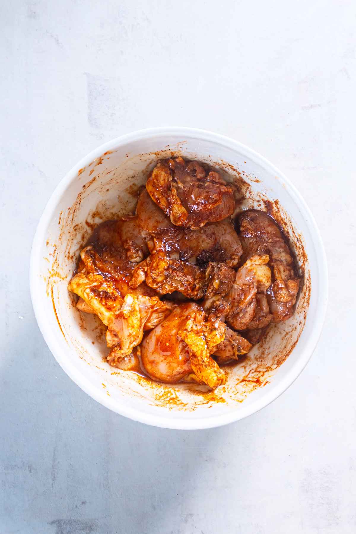 Raw chicken thighs coated in honey chili-lime marinade in a white mixing bowl.