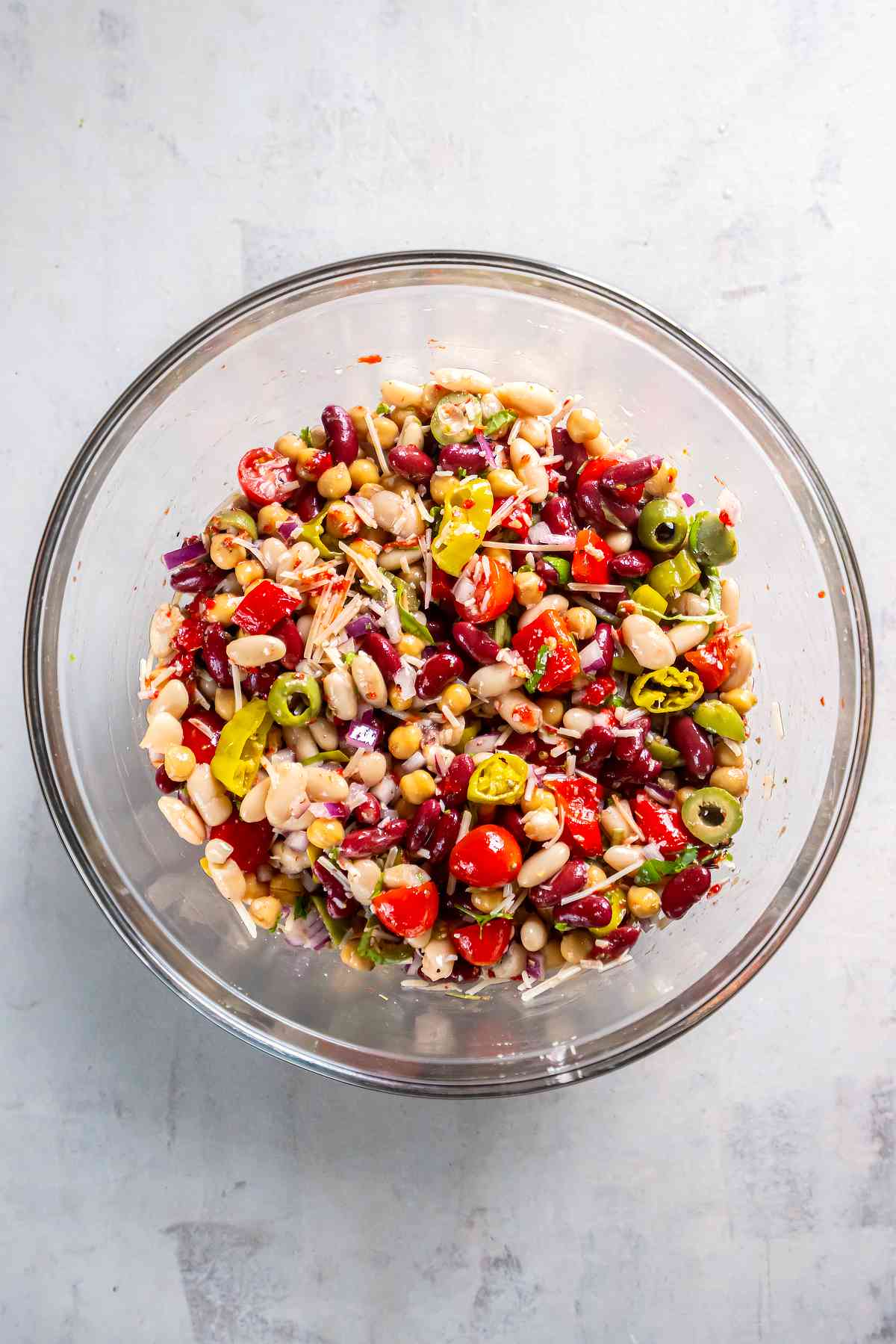 Overhead view of Italian three bean salad mixed with tomatoes, peppers, olives, onion, Parmesan, and herbs.