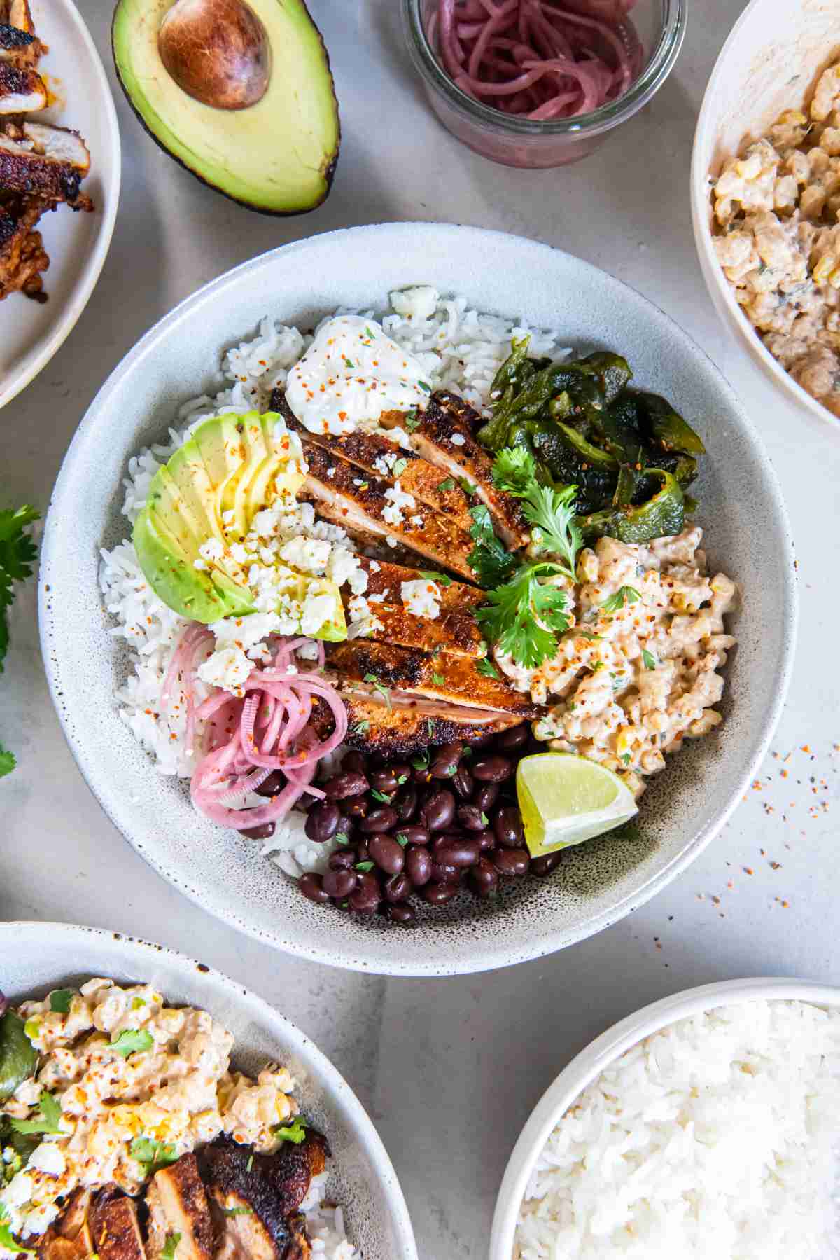 Overhead view of a chicken rice bowl topped with creamy street corn, avocado, black beans, pickled onions, cilantro, Cotija and lime.