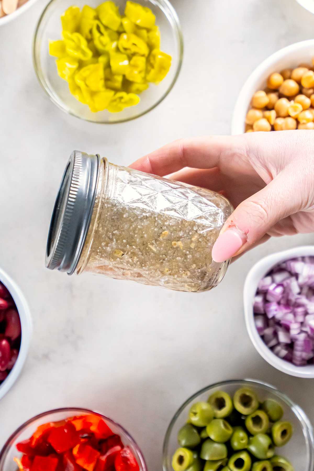 Hand shaking a mason jar of red wine vinaigrette for Italian three bean salad.