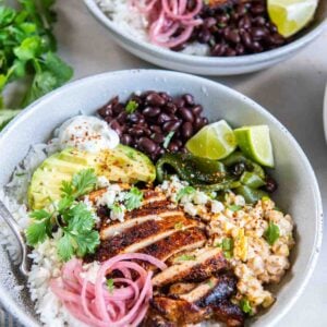 Street corn chicken rice bowl with sliced chili-lime chicken, creamy charred corn, rice, black beans, avocado, pickled onions, Cotija and lime.