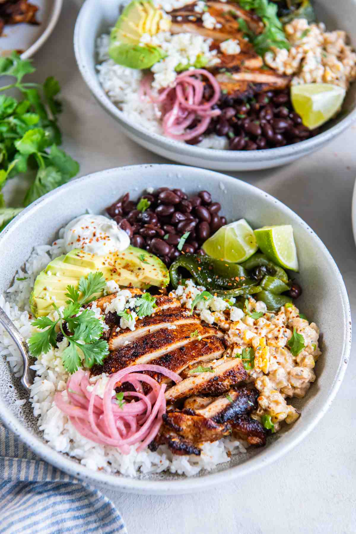 Street corn chicken rice bowl with sliced chili-lime chicken, creamy charred corn, rice, black beans, avocado, pickled onions, Cotija and lime.