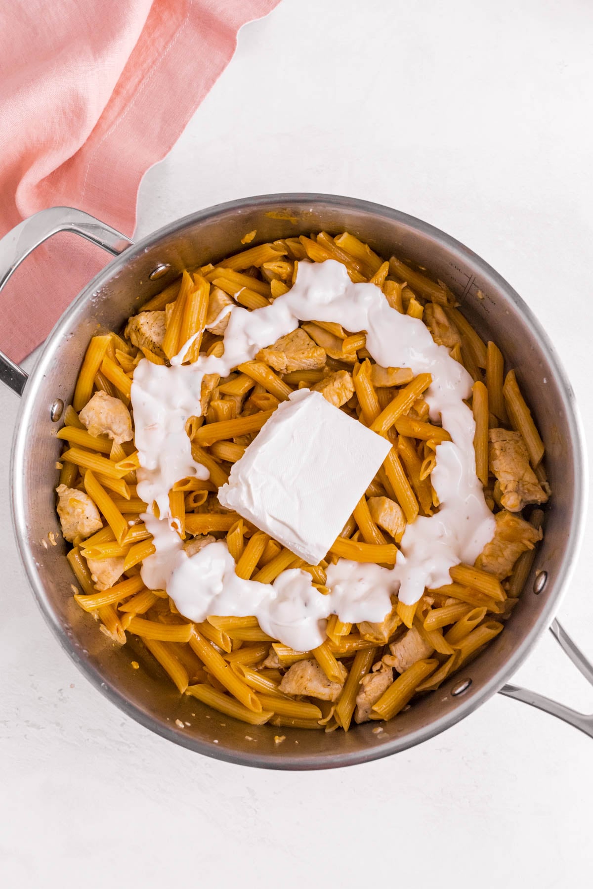Cream cheese and blue cheese dressing added to cooked buffalo chicken pasta in a skillet.