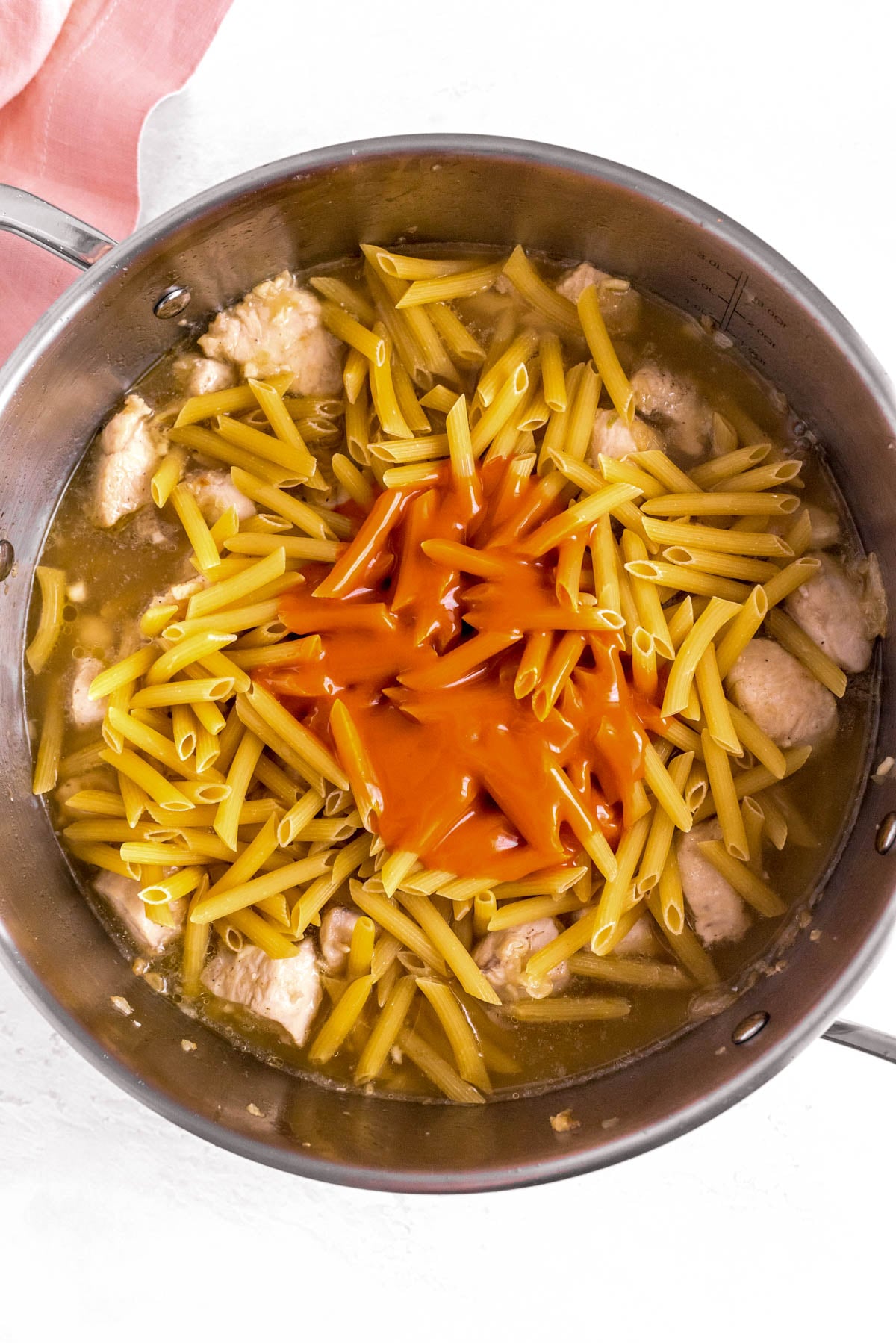 Uncooked penne, chicken broth and buffalo sauce added to browned chicken in a skillet.