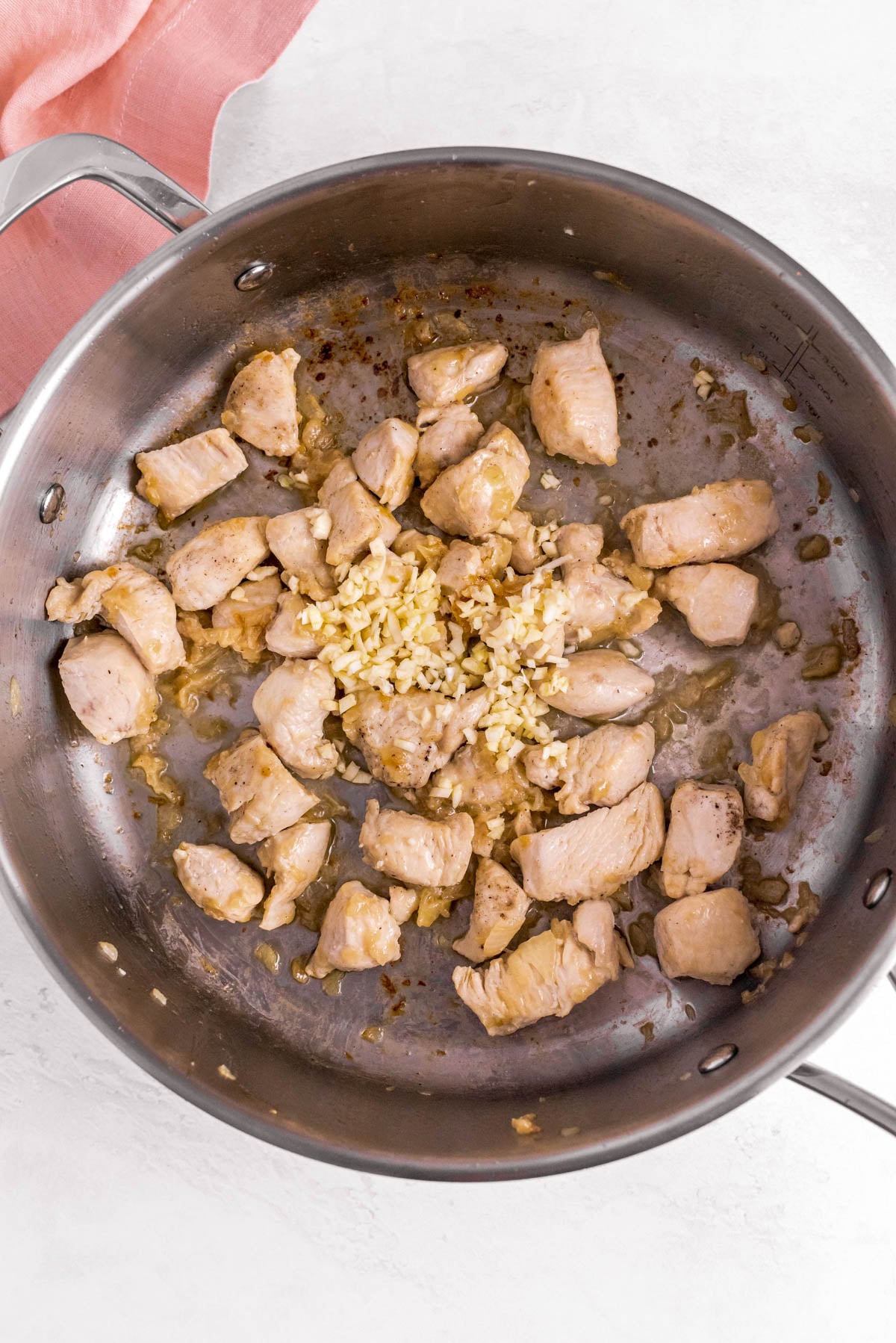 Bite-size chicken pieces browned with onion and minced garlic in a large skillet.