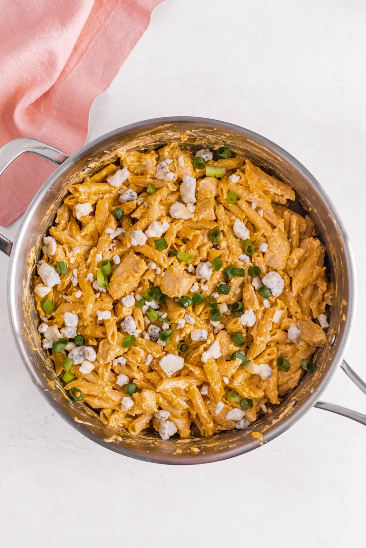 Finished buffalo chicken pasta in a skillet topped with blue cheese crumbles and sliced green onions.