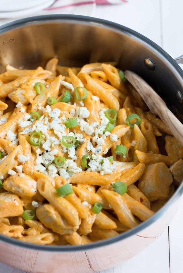 Close-up of creamy one-pan buffalo chicken pasta topped with blue cheese crumbles and sliced green onions.