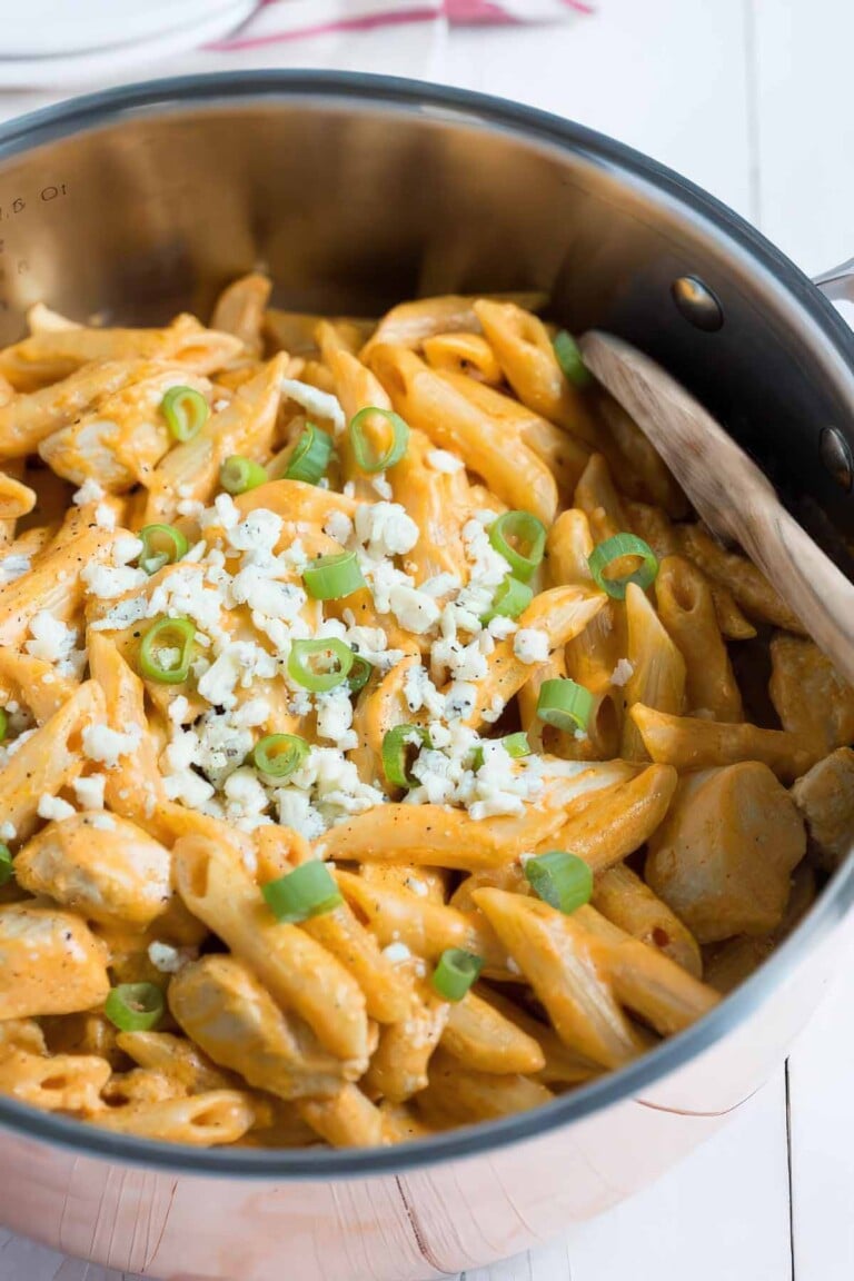 Close-up of creamy one-pan buffalo chicken pasta topped with blue cheese crumbles and sliced green onions.