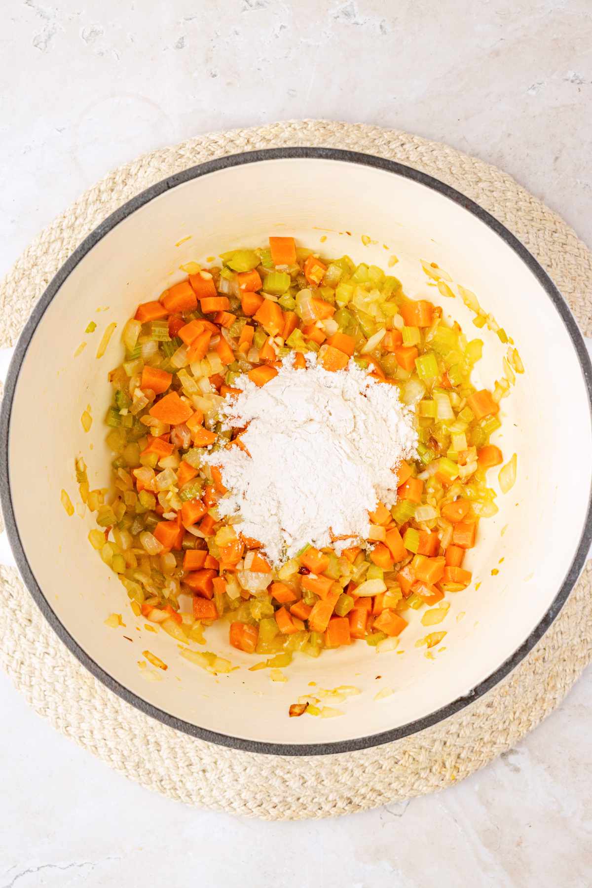 Flour added on top of sautéed carrots, celery, onion and garlic in a white Dutch oven.
