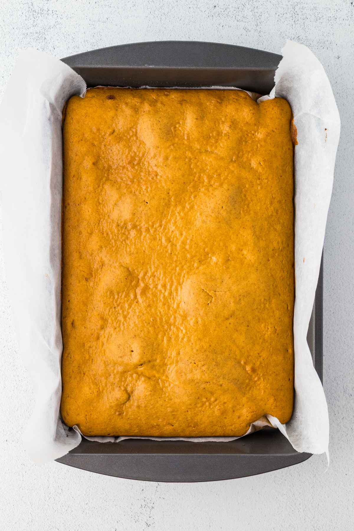 Baked pumpkin bars cooling in a parchment-lined 9x13-inch pan