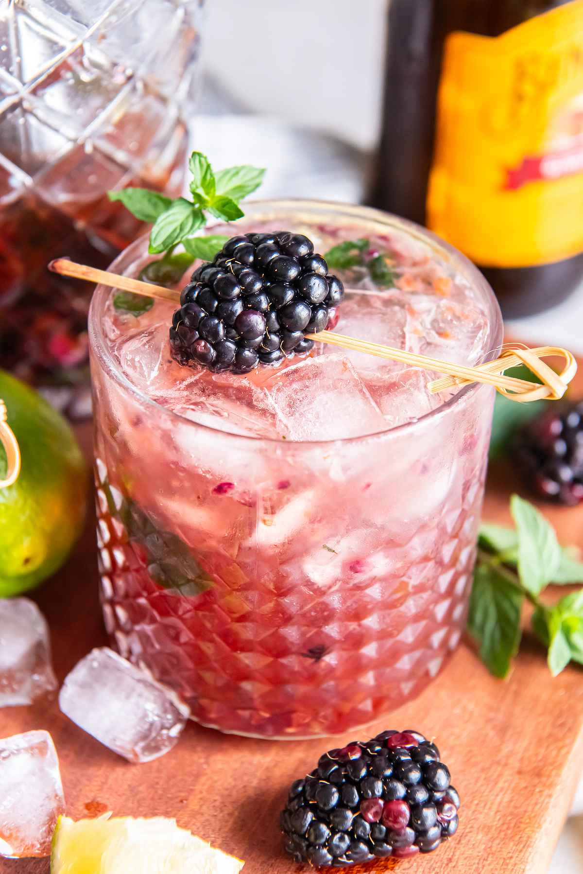 Close-up of a blackberry bourbon smash over ice, garnished with fresh mint and a blackberry on a cocktail pick.