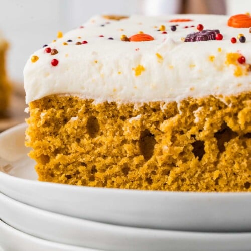Close-up of a soft cake-style pumpkin bar topped with cream cheese frosting and fall sprinkles