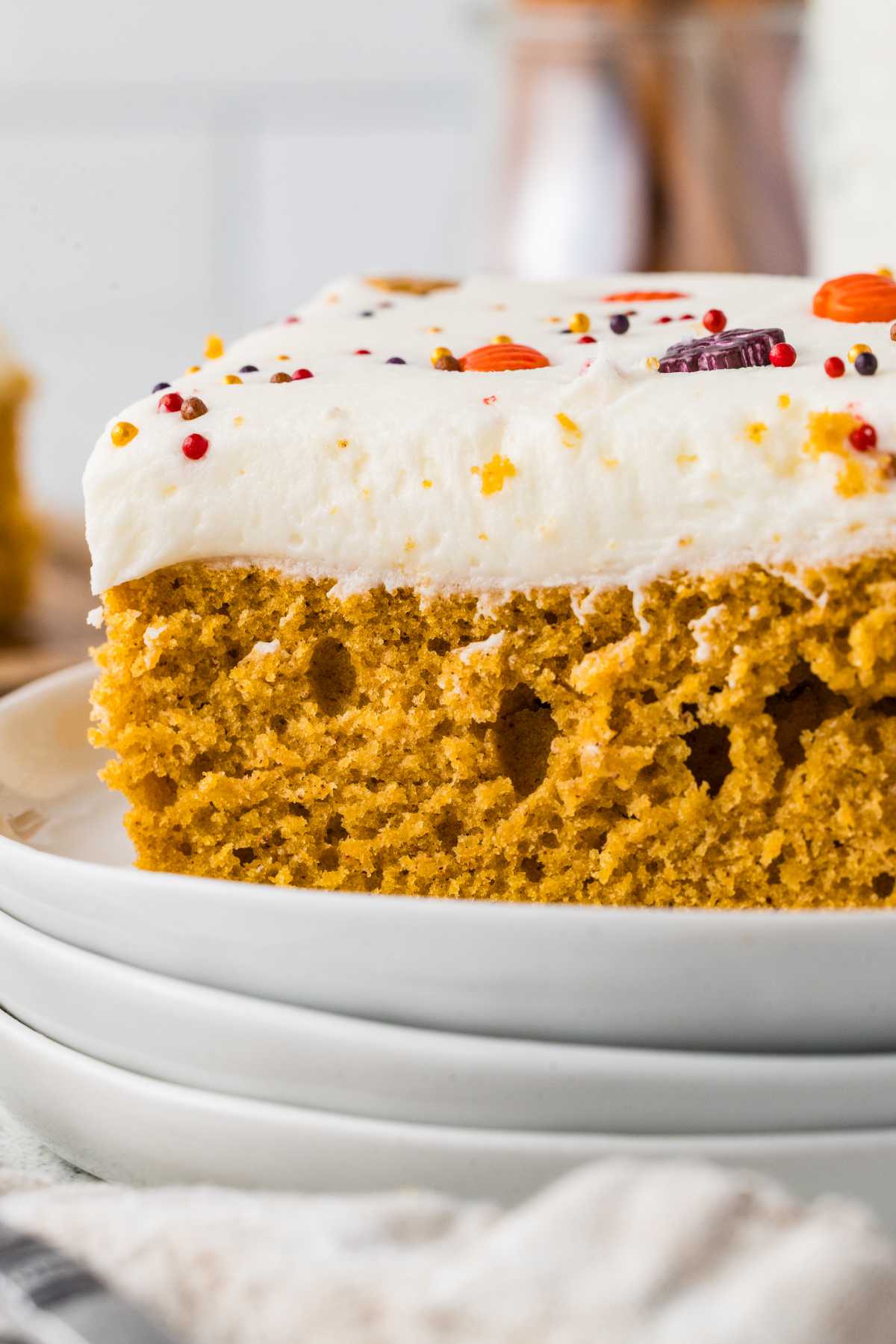 Close-up of a soft cake-style pumpkin bar topped with cream cheese frosting and fall sprinkles