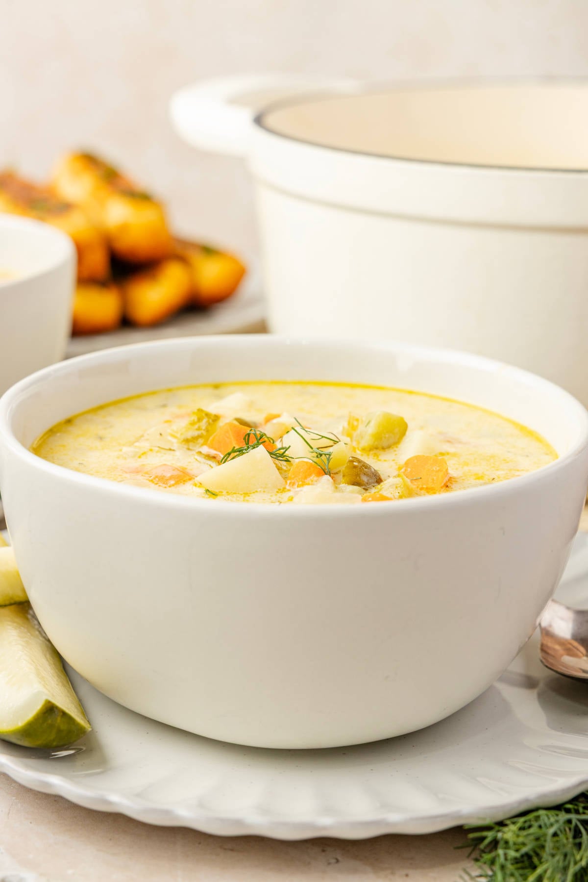 Side view of creamy dill pickle soup topped with fresh dill, with potatoes, carrots and chopped pickles in a white bowl.