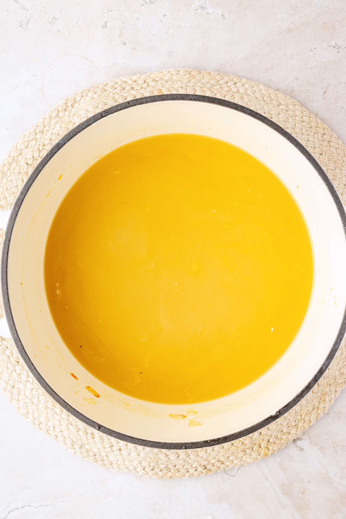 Golden broth covering the sautéed vegetables in a white Dutch oven.