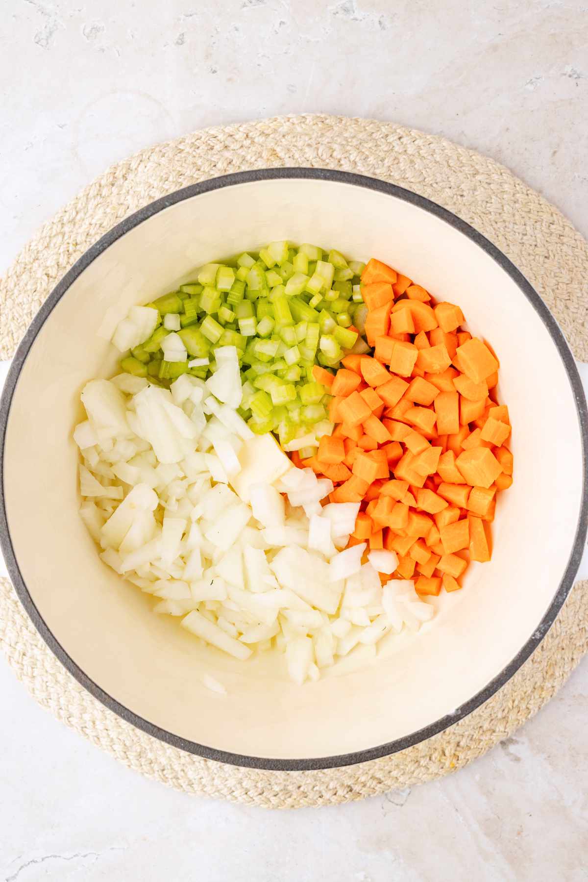 Diced carrots, celery and onion arranged in a white Dutch oven before sautéing.
