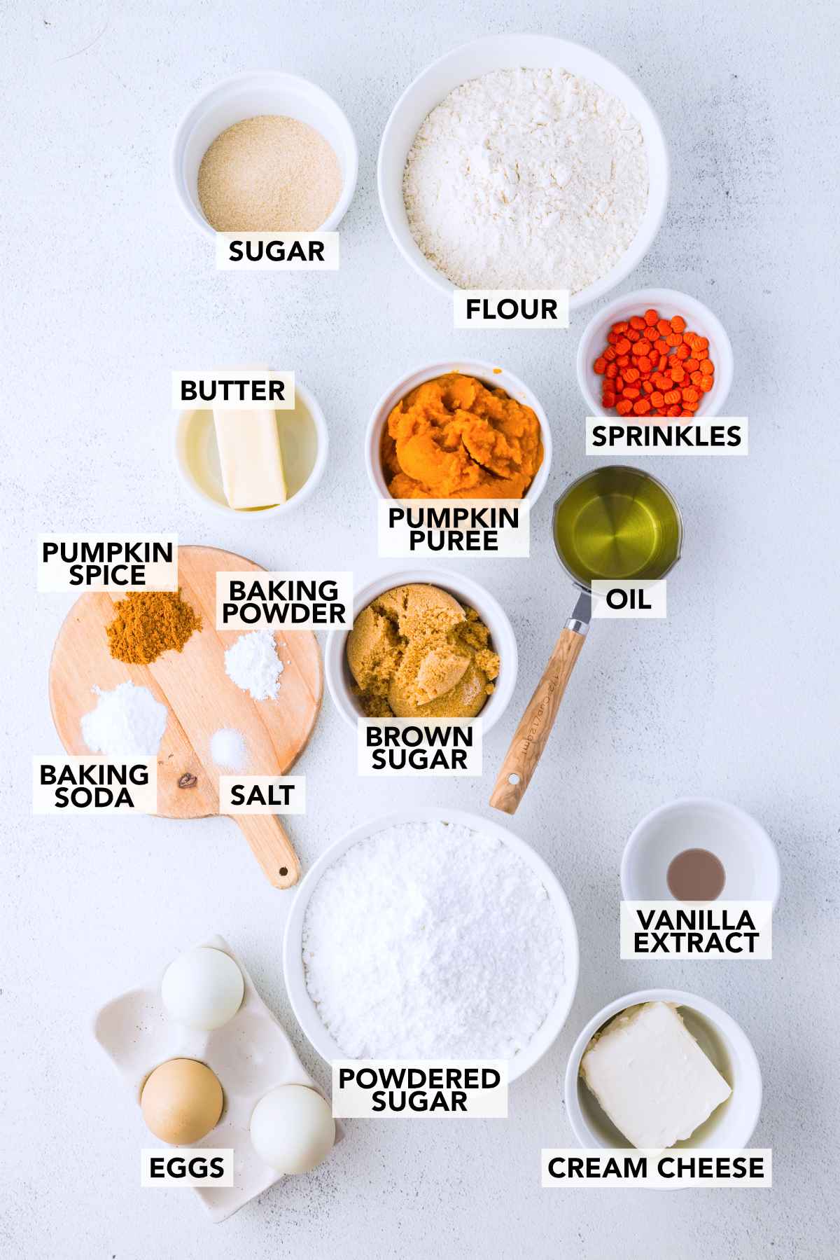 Labeled ingredients for pumpkin bars with cream cheese frosting, including pumpkin puree, flour, eggs, vegetable oil and warm spices