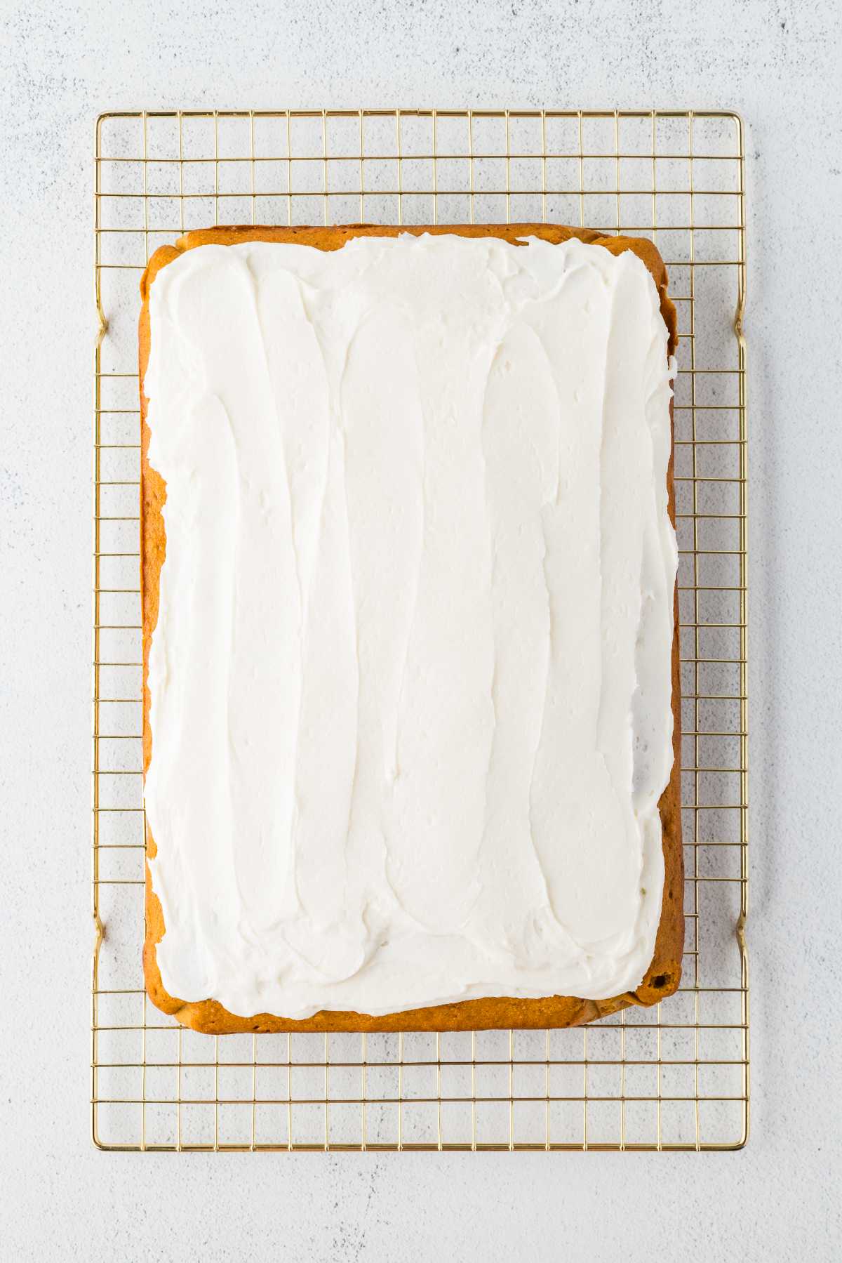 A pan of pumpkin bars covered with a thick layer of vanilla cream cheese frosting on a cooling rack