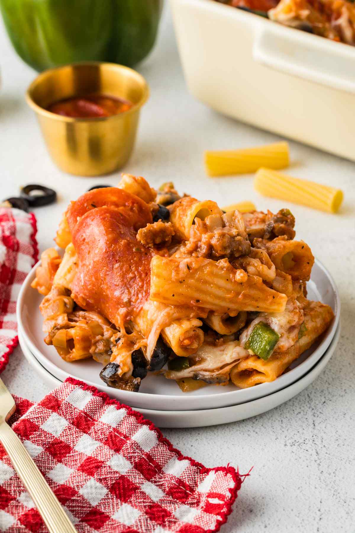 Pizza casserole served on a white plate with rigatoni, sausage, pepperoni, mushrooms, olives, green peppers, and melted cheese.