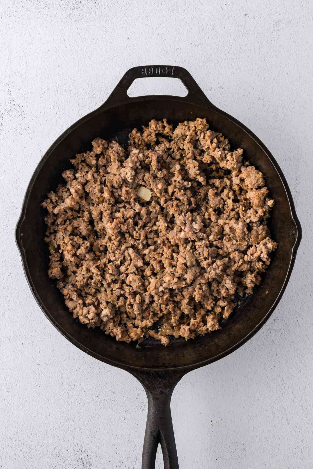 Browned ground sausage broken into crumbles in a cast-iron skillet.