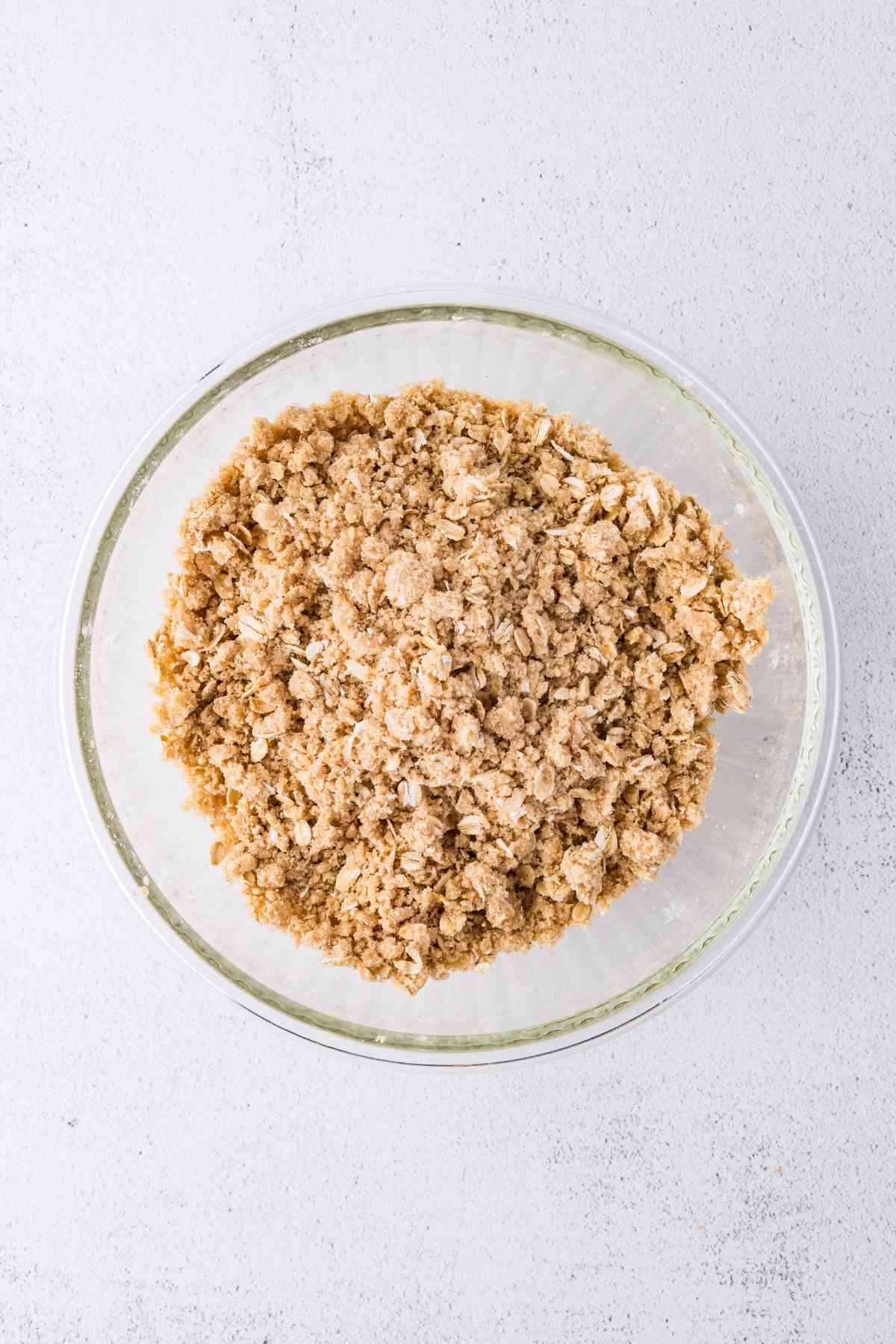 Oats, flour, brown sugar, butter and cinnamon combined into crumbly topping in a glass bowl.