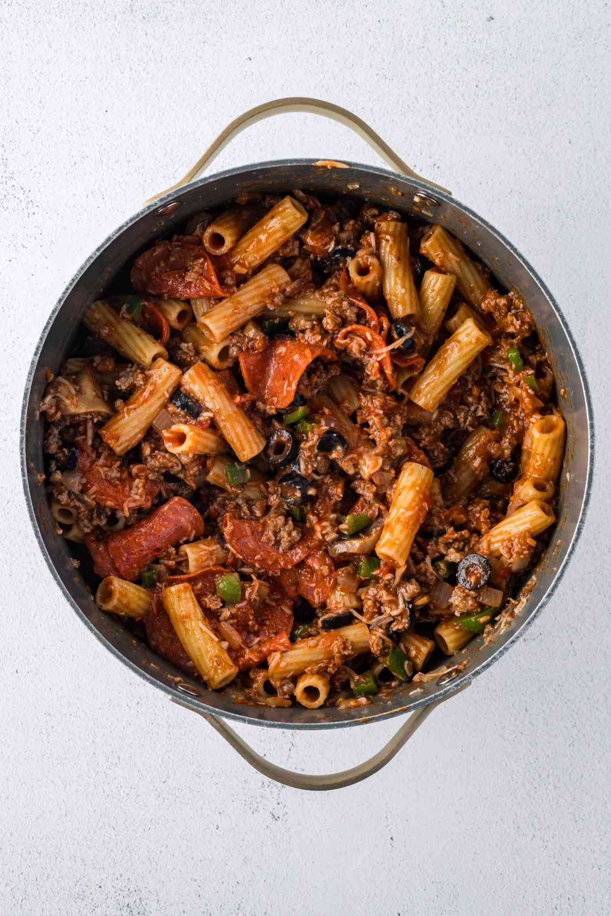Rigatoni mixed with marinara, sausage, pepperoni, mushrooms, black olives, green peppers, onions, and cheese in a pot.