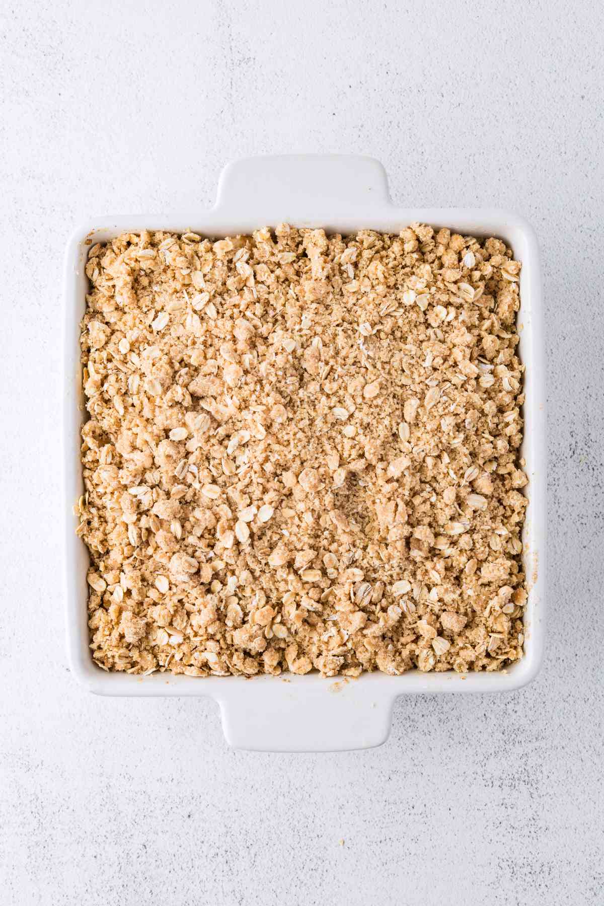 Unbaked pear crisp covered with an even layer of oat crumble in a square white baking dish.