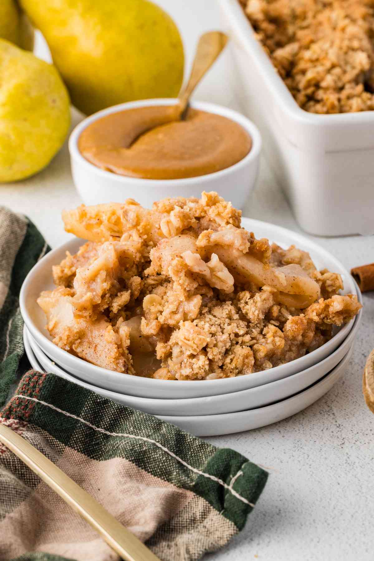 Sliced pears and golden oat crumble piled in a white bowl, with caramel sauce alongside.