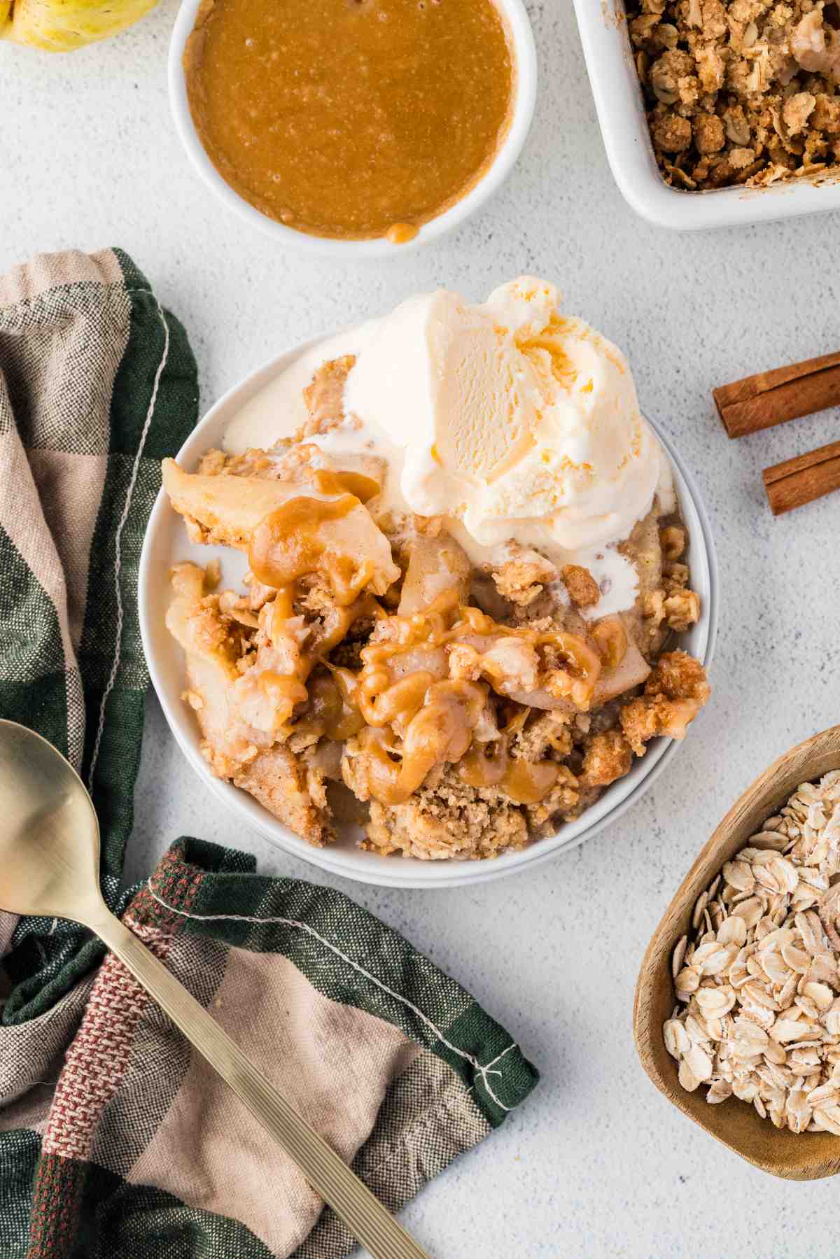Overhead view of pear crisp topped with caramel sauce and vanilla ice cream in a white bowl.