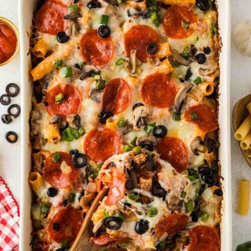 A wooden spoon lifting a serving of pizza casserole from a baking dish topped with pepperoni, melted cheese, and vegetables.