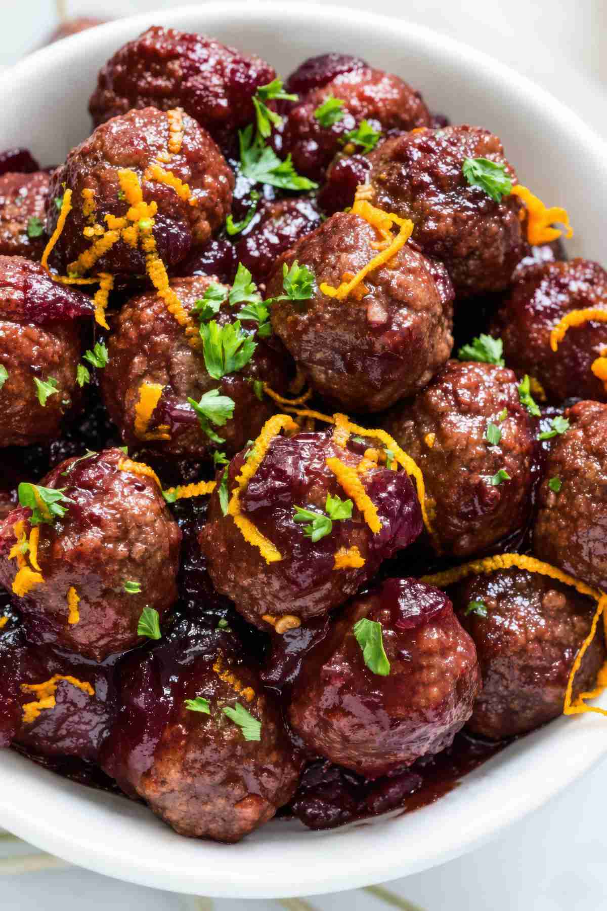 Close-up of slow cooker cranberry meatballs coated in whole berry cranberry sauce and garnished with parsley and orange zest.