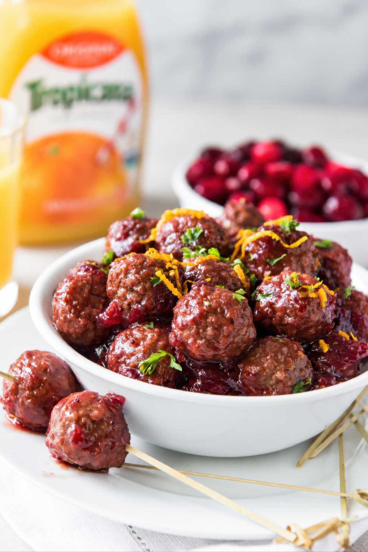 Slow cooker cranberry meatballs garnished with parsley and orange zest in a white bowl, with skewered meatballs on the plate.